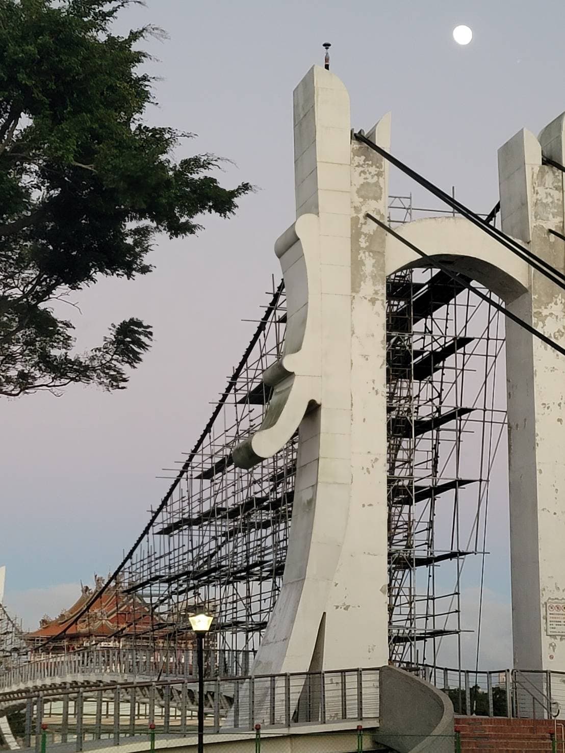 柏凱鷹架工程於龍潭大池吊橋主塔進行高空鷹架架設，背景清晰可見龍潭南天宮，展現精準的立體結構搭設技術。