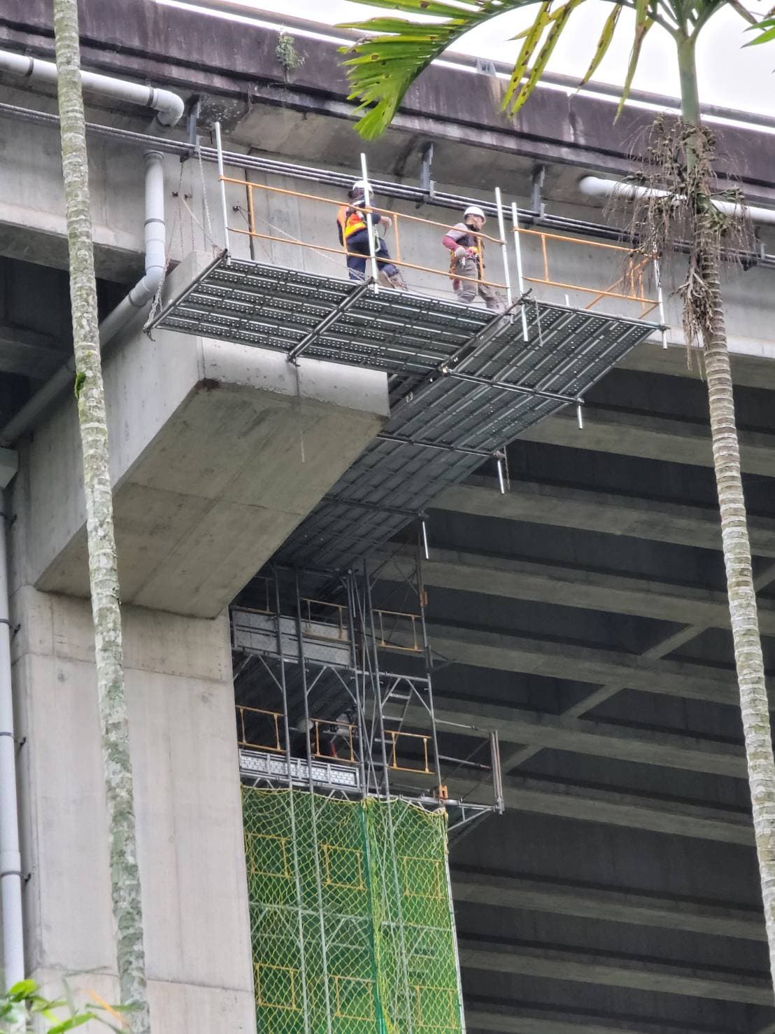 柏凱鷹架工程於北二高橋樑補強工地現場，兩名配戴安全防護裝備的施工人員，正在國道三號橋墩旁的懸吊式施工架工作平台上進行結構維護作業。